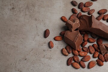 Pieces of tasty milk chocolate and cocoa beans on grey table, above view. Space for text