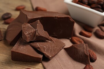 Pieces of tasty milk chocolate and cocoa beans on table, closeup
