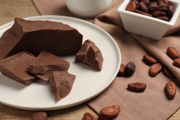 Pieces of tasty milk chocolate and cocoa beans on table, closeup