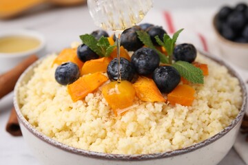 Pouring honey onto tasty couscous with blueberries, pumpkin and mint, closeup