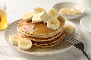 Delicious pancakes with bananas, honey and butter on white wooden table, closeup