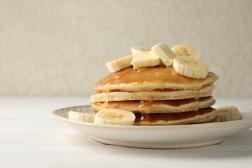 Delicious pancakes with bananas, honey and butter on white wooden table, closeup. Space for text