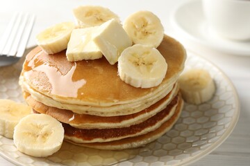 Delicious pancakes with bananas, honey and butter on white wooden table, closeup