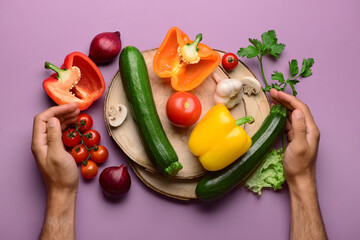 Man with wooden boards, fresh vegetables and greenery on purple background