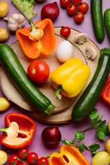 Wooden boards with fresh vegetables and greenery on purple background