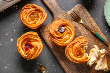 Wooden board of tasty cruffins with chocolate and jam on black background