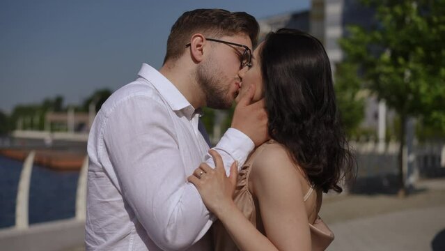 Close-up. A man tenderly kisses a woman on the lips while standing on the city embankment