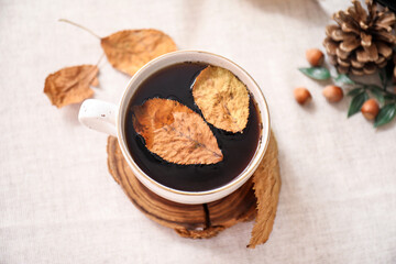 Cup of tea with autumn leaves on white table, closeup