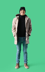 Young man in winter clothes on green background