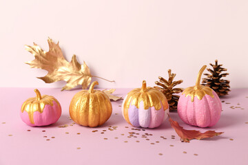Different painted pumpkins with golden leaves and cones on colorful background