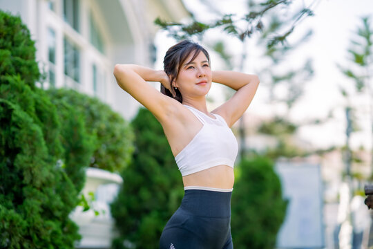Happy slim woman wearing sportswear jogging and stretch the muscles to warm up the body in the city at sunrise. Young beautiful asian female in sports bra running outdoor.Healthy and active lifestyle 