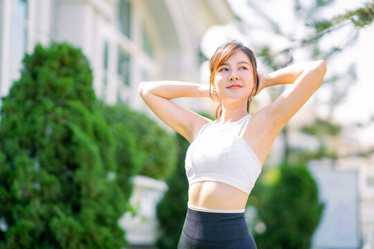 Happy slim woman wearing sportswear jogging and stretch the muscles to warm up the body in the city at sunrise. Young beautiful asian female in sports bra running outdoor.Healthy and active lifestyle 