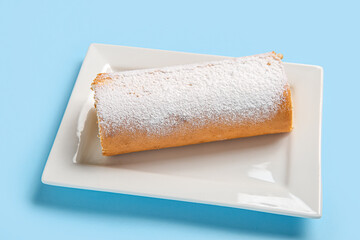 Plate with sweet sponge cake roll on blue background