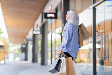 An Asian Muslim woman is carrying a bag of goods that she has been shopping for and buying a lot of...