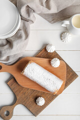 Boards with sweet sponge cake roll and meringue on white wooden background
