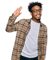 Naklejka premium Young african american man with beard wearing casual clothes and glasses waiving saying hello happy and smiling, friendly welcome gesture