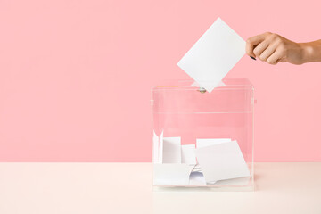 Hand putting voting paper in ballot box on pink background