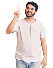 Young hispanic man wearing casual clothes showing and pointing up with finger number one while...