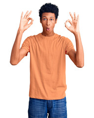 Fototapeta premium Young african american man wearing casual clothes looking surprised and shocked doing ok approval symbol with fingers. crazy expression
