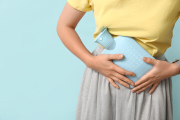 Young woman with hot water bottle having menstrual cramps on blue background, closeup