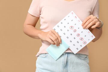 Young woman with menstrual pad and calendar on beige background, closeup