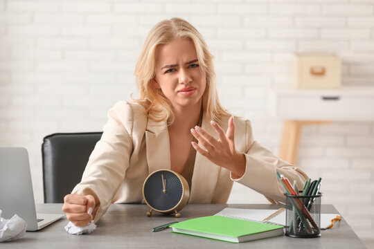 Young displeased businesswoman with alarm clock trying to meet deadline in office. Time management concept
