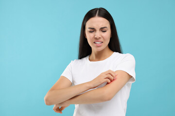 Suffering from allergy. Young woman scratching her arm on light blue background