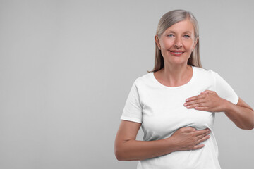 Beautiful senior woman doing breast self-examination on light grey background, space for text