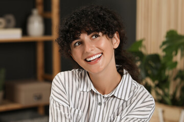 Portrait of beautiful woman with curly hair indoors. Attractive lady smiling and posing for camera
