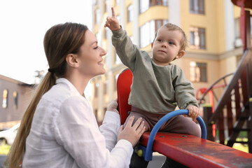 Happy nanny and cute little boy on seesaw outdoors - obrazy, fototapety, plakaty