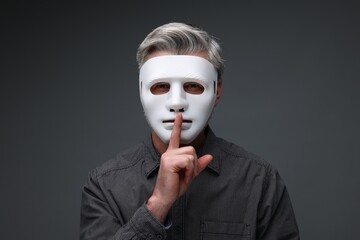 Man in mask showing hush gesture against dark grey background