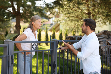 Emotional neighbours having argument near fence outdoors