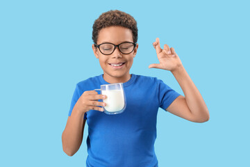 Little African-American boy with glass cup of milk and crossed fingers on blue background