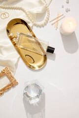 Fashion composition with accessories on white background. Pearl necklace, ring, scented candle and fabric decorated. A glass perfume bottle unlabeled displayed on gold tray. Mockup for design