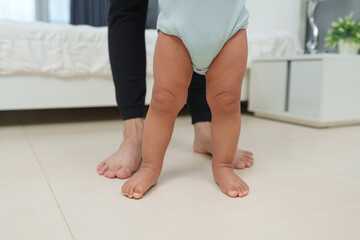 close up leg of infant baby walking with mother helping