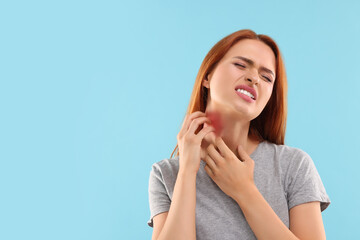 Suffering from allergy. Young woman scratching her neck on light blue background, space for text