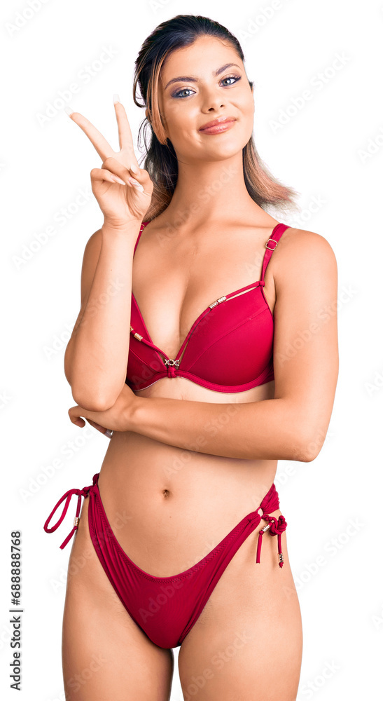 Poster Young beautiful woman wearing bikini smiling looking to the camera showing fingers doing victory sign. number two.