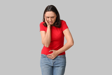 Beautiful young woman suffering from menstrual cramps on grey background