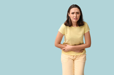 Beautiful young woman suffering from menstrual cramps on blue background