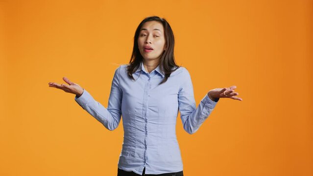 Doubtful model raising shoulders over orange background, showing doubt and being clueless about answer. Young filipino person acting uncertain and confused standing in front of camera.