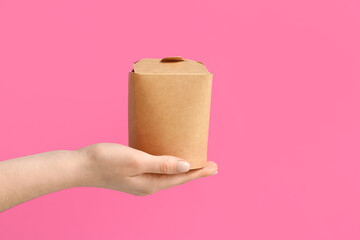 Female hand with takeaway paper box on pink background