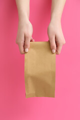 Female hands with takeaway paper bag on pink background