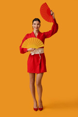 Beautiful young happy woman with fans on yellow background. Chinese New Year celebration