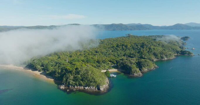 Rotating aerial view of remote and rugged Ulva Island, part of Stewart Island Rakiura, in the south of New Zealand Aotearoa, with moored boat in secluded white sandy beach bay
