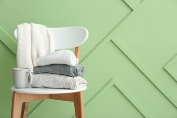 Chair with different stylish sweaters and cup of tea near green wall in room