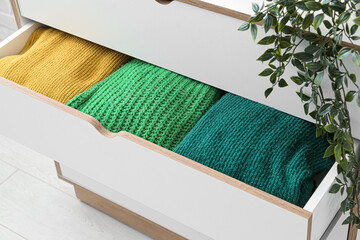 Chest of drawers with different stylish sweaters and houseplant in room, closeup