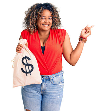 Young african american plus size woman holding money bag with dollar symbol smiling happy pointing with hand and finger to the side