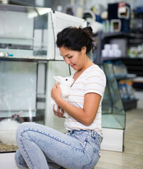 Portrait of smiling woman choosing new pet in store, holding cute rabbit