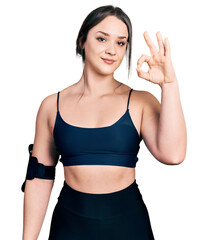 Young hispanic woman wearing sportswear smiling positive doing ok sign with hand and fingers. successful expression.