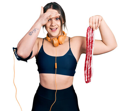 Young hispanic girl wearing sportswear holding meat stressed and frustrated with hand on head, surprised and angry face